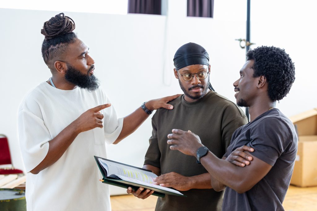 three men stood together in a room, facing each other and reading from a piece of paper in front of them
