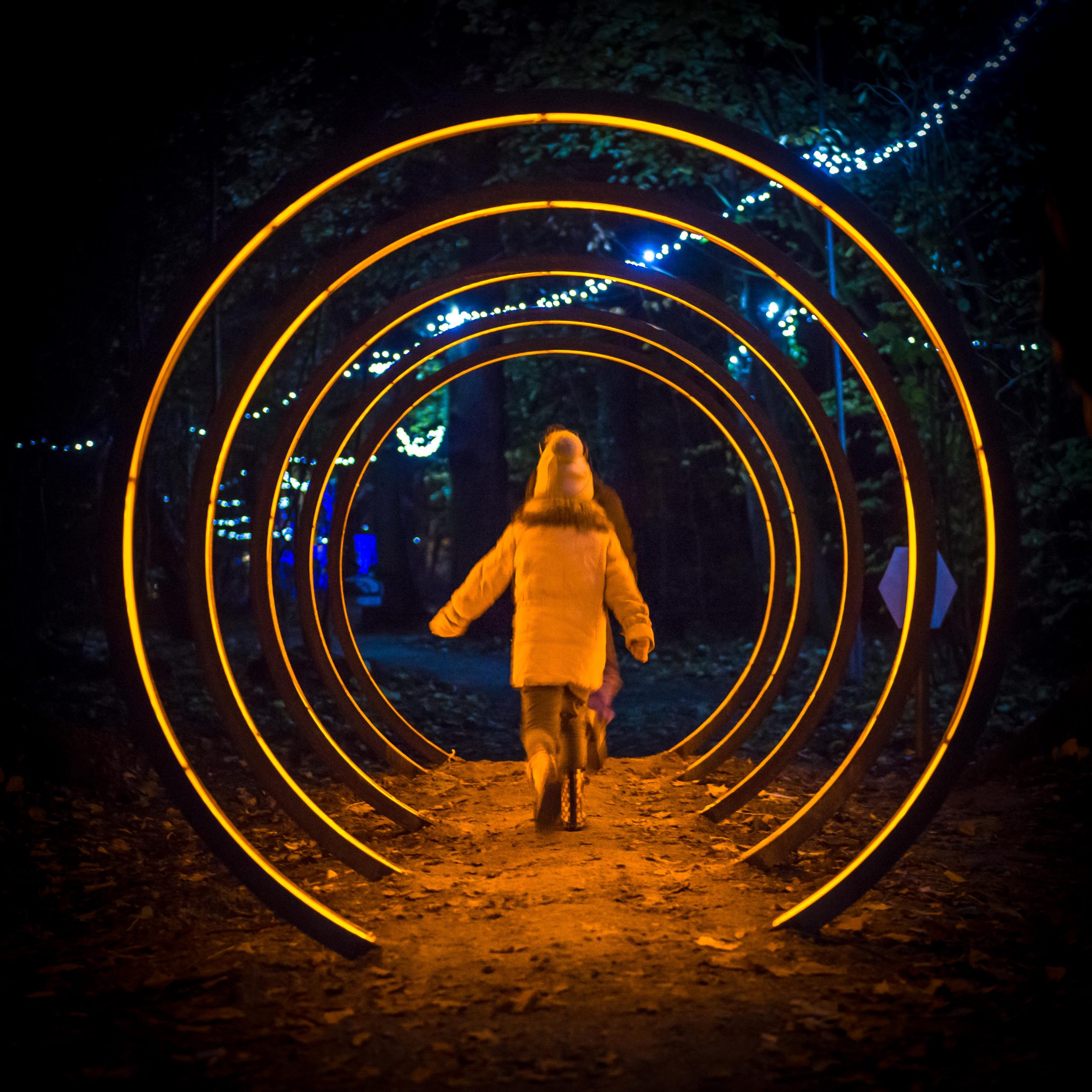 a night time shot with a child in a winter coat and hat walking through a light up circle installation