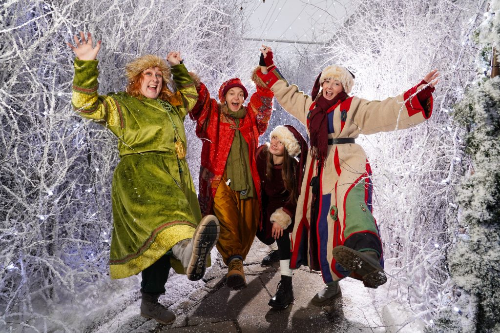 four people in a snowy landscape dressed in elf costumes, with greens and reds