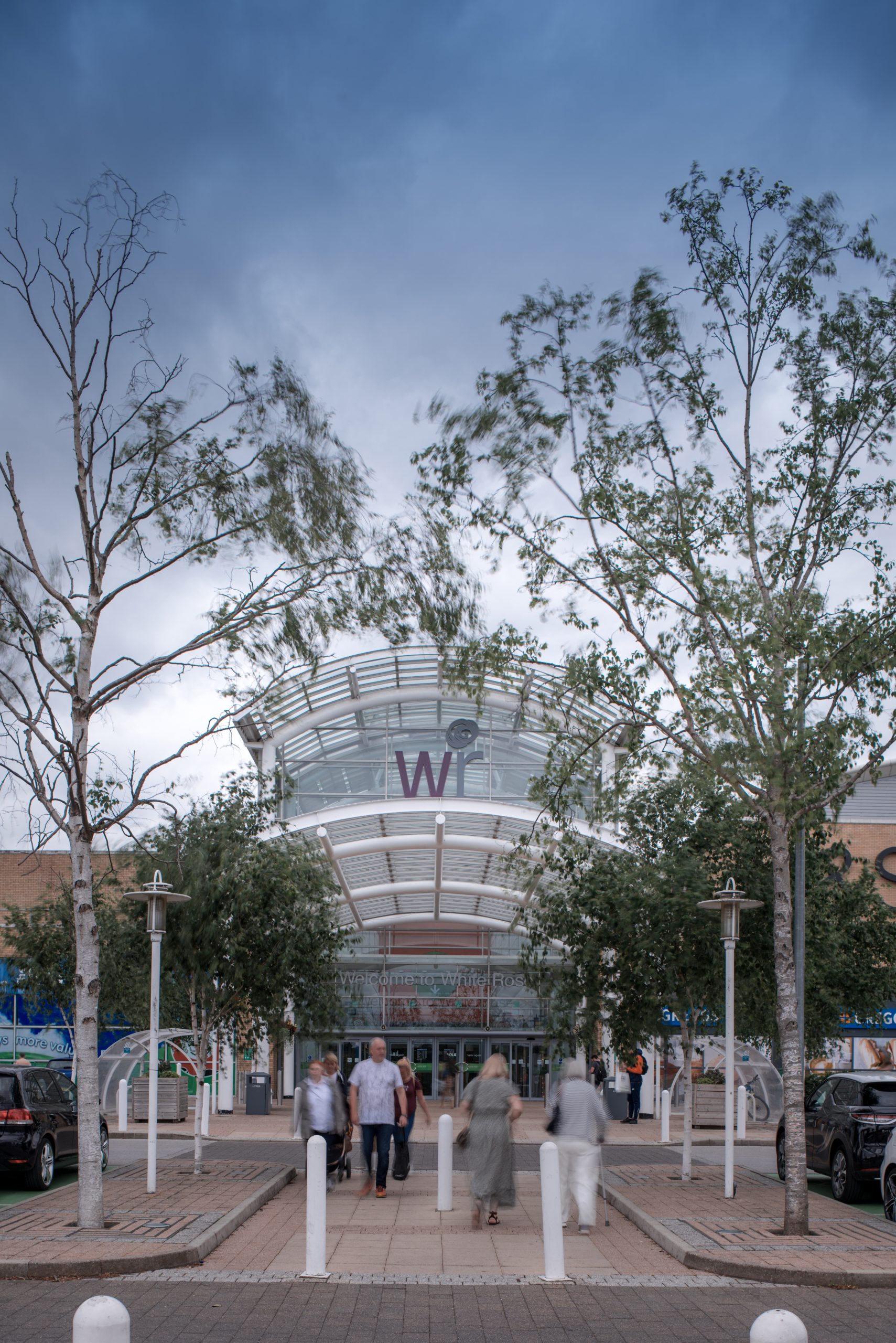 the front entrance of a shopping centre with trees lining the path