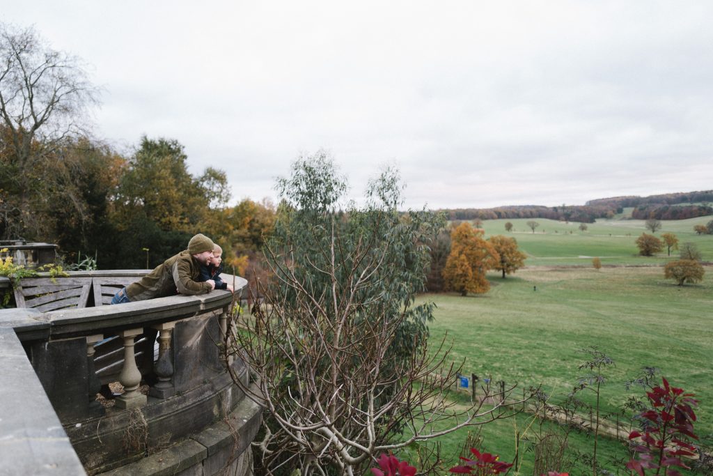 a stone terrace over a field and trees with a a man and child looking out 