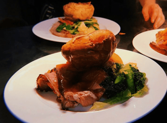 a plate with a full sunday roast and yorshire pudding on top sitting under a hot light