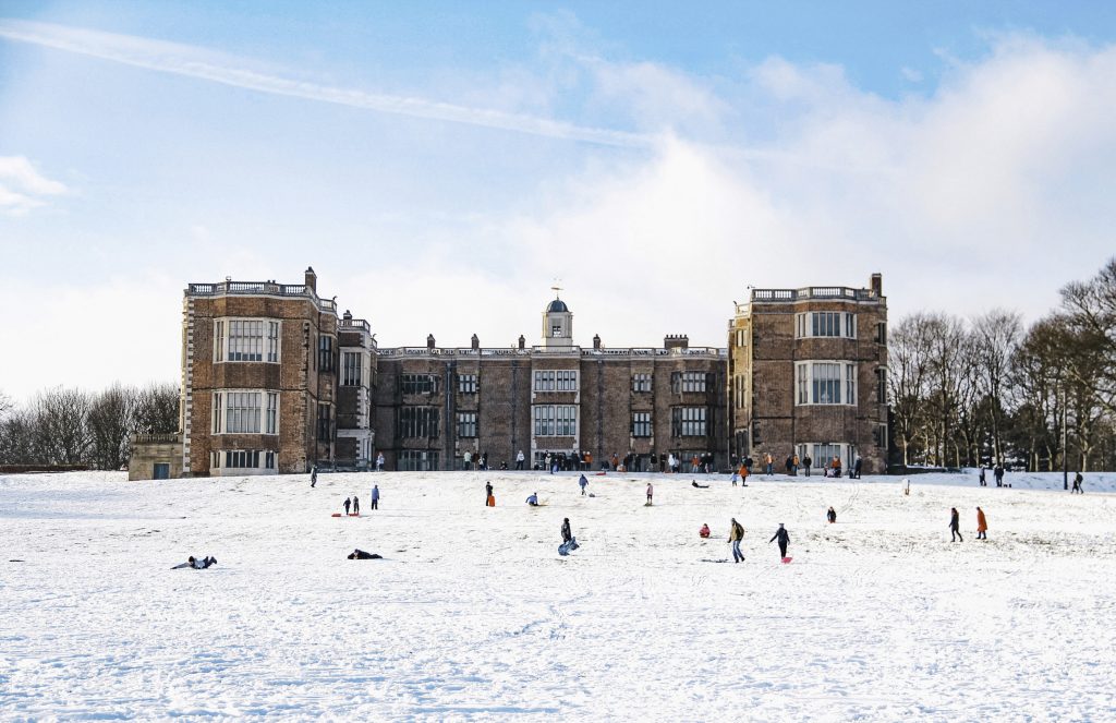 a snowy landscape in front of a large historic home with people sledding down a snowy hill in front