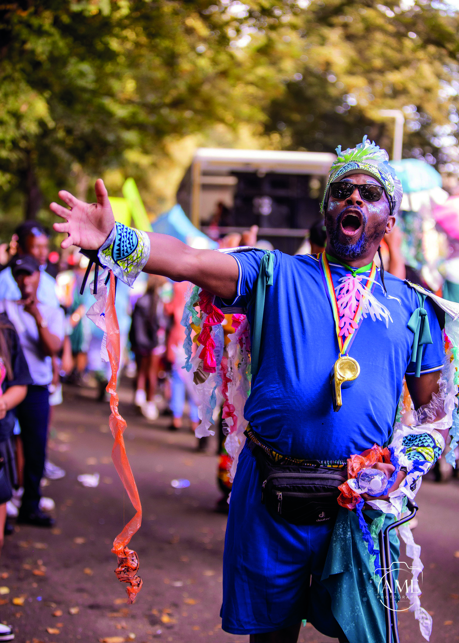 a man in colourful outfit outside with a parade crowd behind him