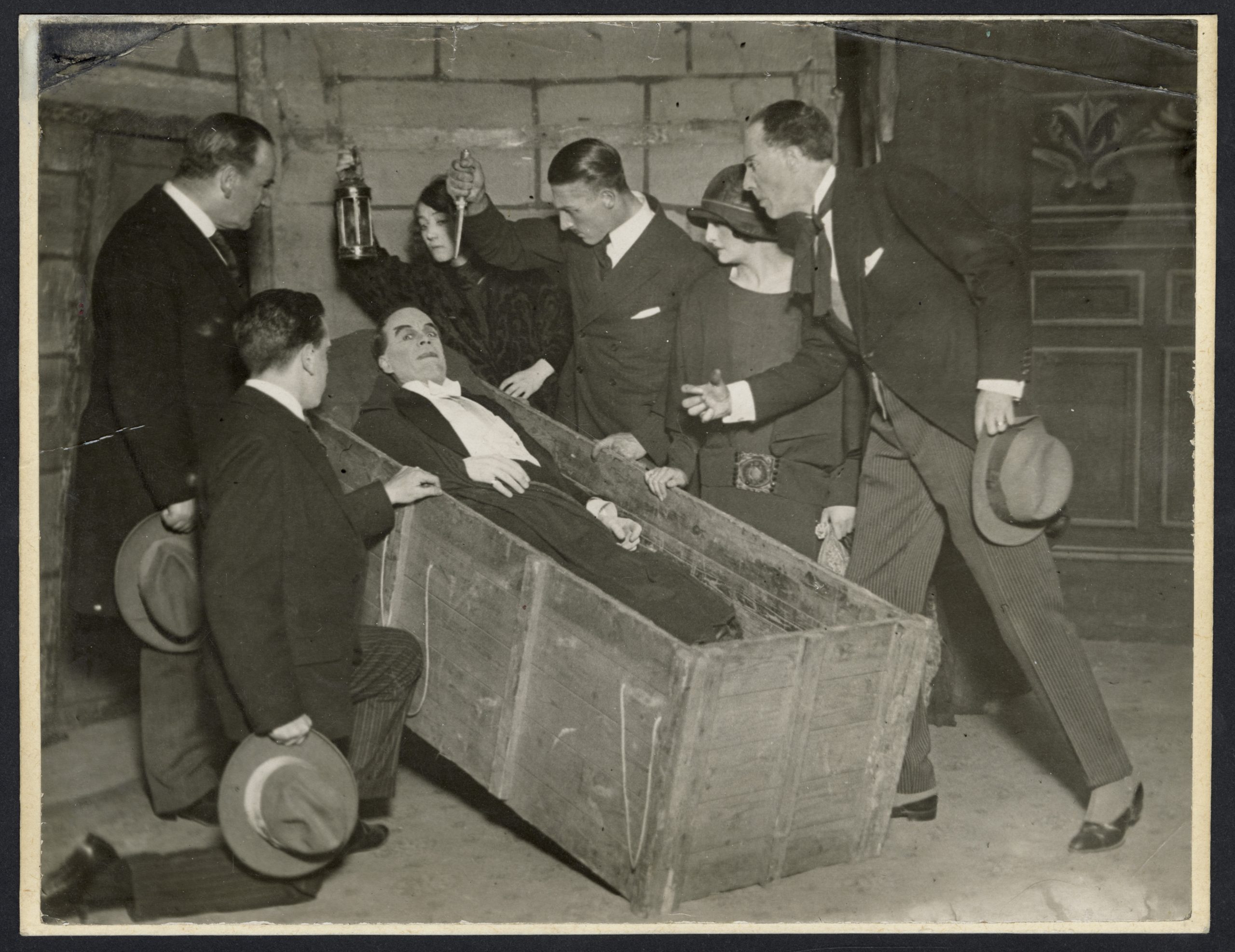 a black and white photograph of several men stood around a man in a wooden coffin