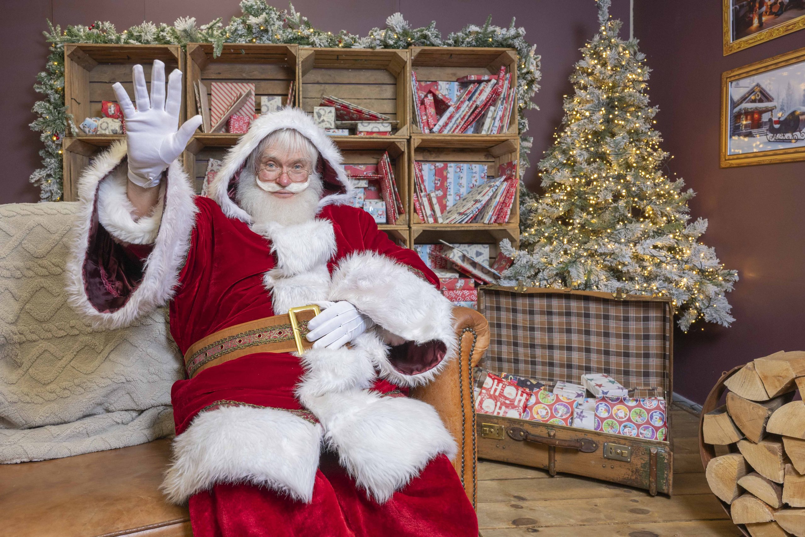santa claus with his red outfit and large white beard sat inside a cabin like room filled with presents and christmas decorations