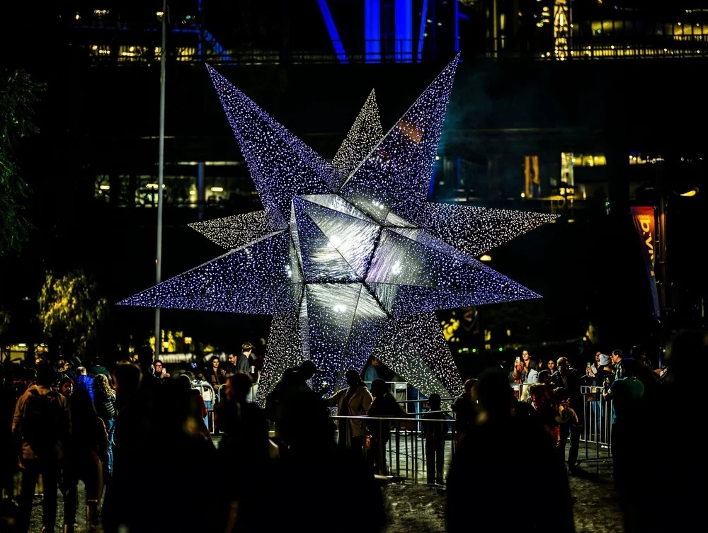 people stood outside at nighttime around a large 3d light up star
